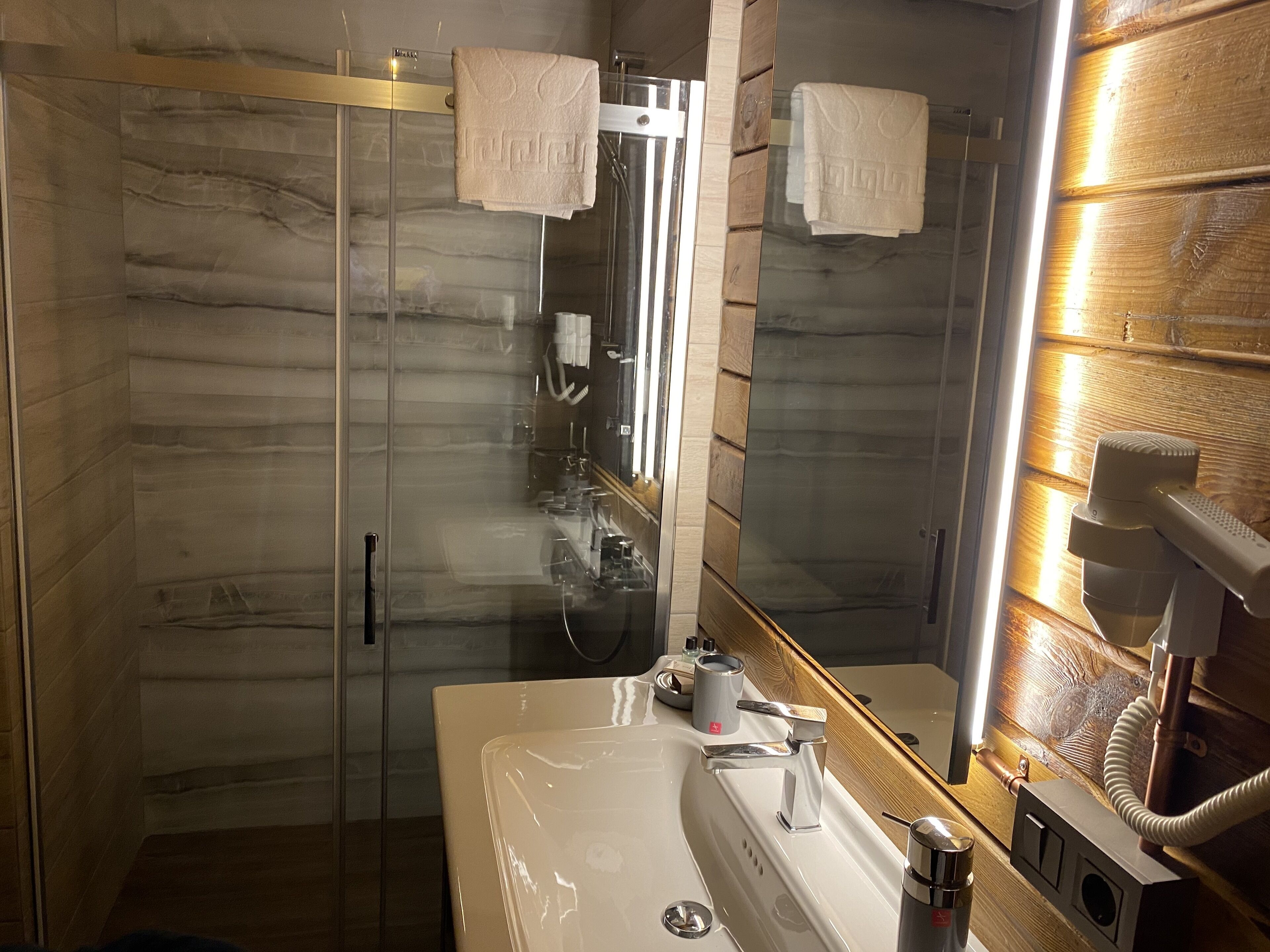 A modern bathroom with a glass-enclosed shower, a sink with a mirror, and a hairdryer on the wall.