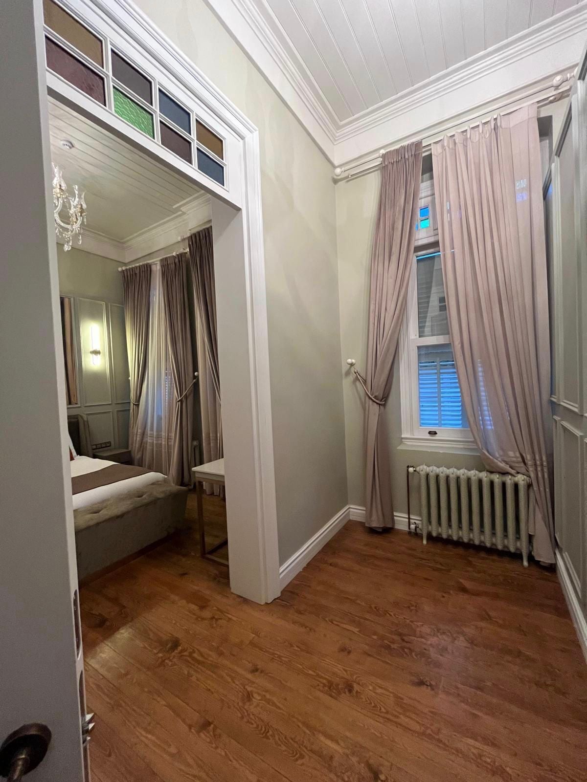 A bedroom with a bunk bed, a radiator, and a window with curtains.