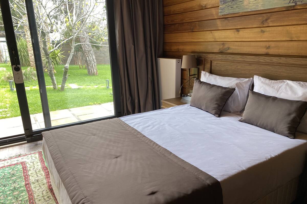 A bedroom with a large bed, a nightstand, a lamp, and a view of a garden through a sliding door.