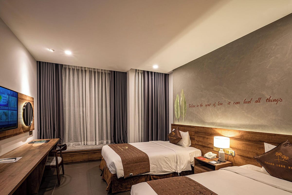 A hotel room with two beds, a desk, a television, and a wall with a motivational quote.