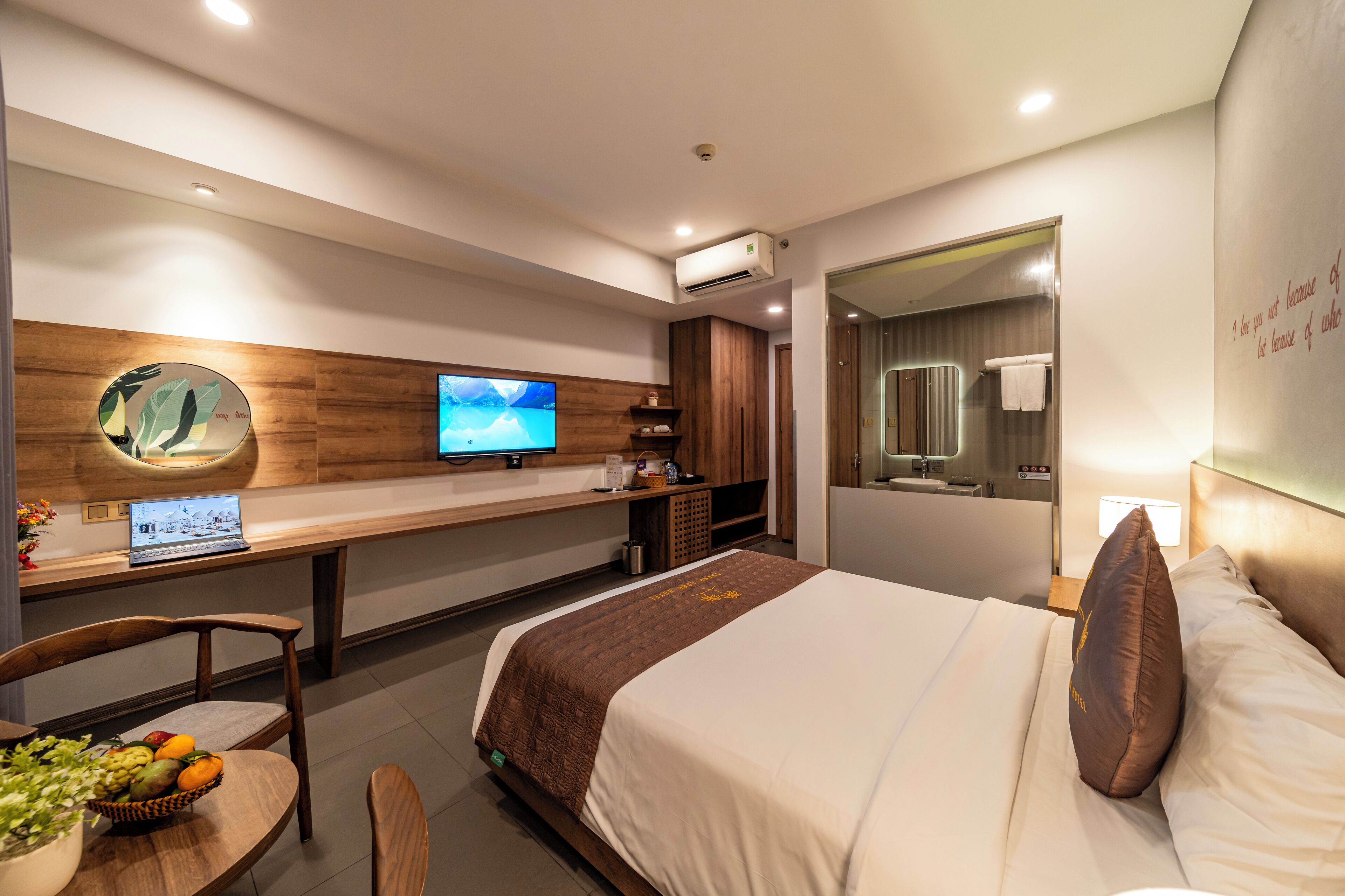 Una habitación de hotel moderna con cama, escritorio con computadora portátil, televisión y barra de desayuno.