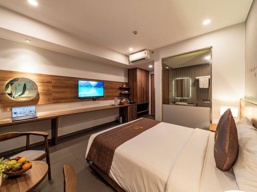 Una habitación de hotel moderna con cama, escritorio con computadora portátil, televisión y barra de desayuno.