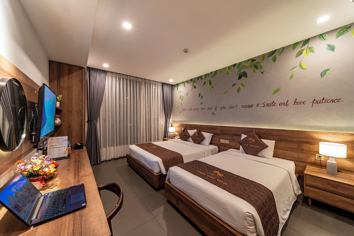 A hotel room with two beds, a desk with a laptop, a TV, and a wall with a motivational quote.