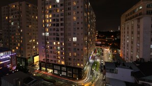 Un edificio alto con varios pisos, ventanas iluminadas y una calle con vehículos en movimiento.