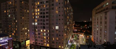 A high-rise building with multiple floors, illuminated windows, and a street with moving vehicles.