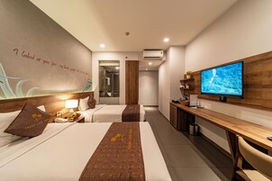 A hotel room with two beds, a TV, a desk, and a bathroom visible through an open door.