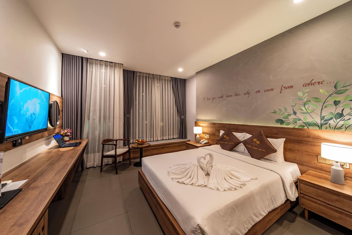 A hotel room with a large bed, a desk with a laptop, a TV, and a wall with a decorative phrase.