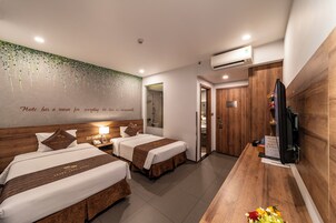A hotel room with two beds, a wooden desk, a television, and a wall with a quote.