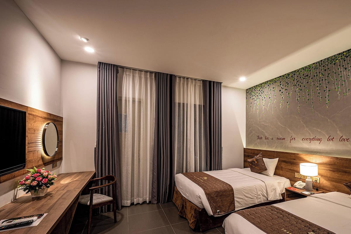 A hotel room with two beds, a desk with a chair, a mirror, and a wall with a quote.