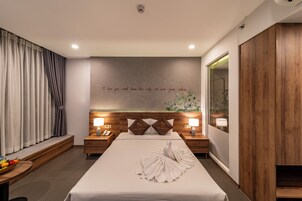 A modern hotel room with a large bed, wooden headboard, bedside lamps, a fruit basket, and a wall with a motivational quote.
