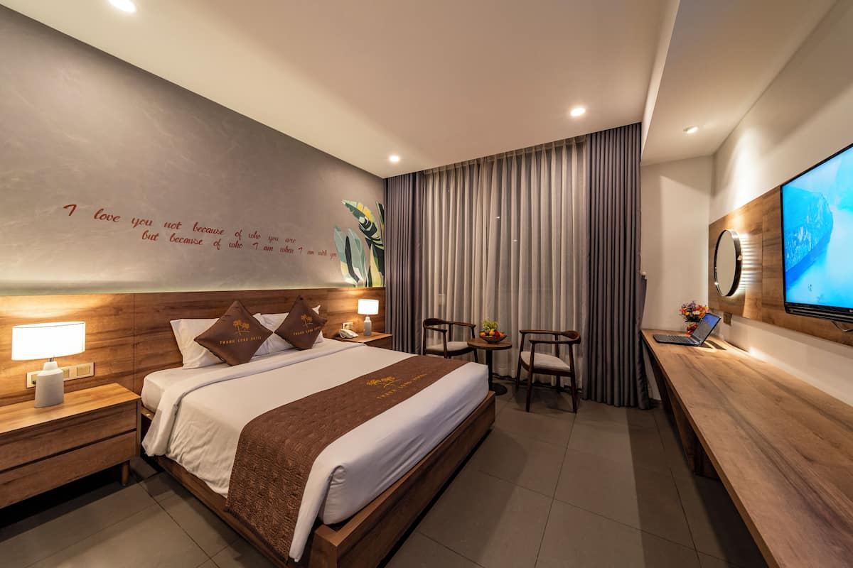 A modern hotel room with a large bed, bedside tables with lamps, a desk with a laptop, and a TV on the wall.