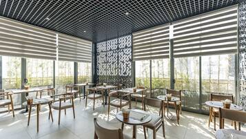 Ein modernes Café mit Holztischen und -stühlen, großen Fenstern und einer gemusterten Decke.