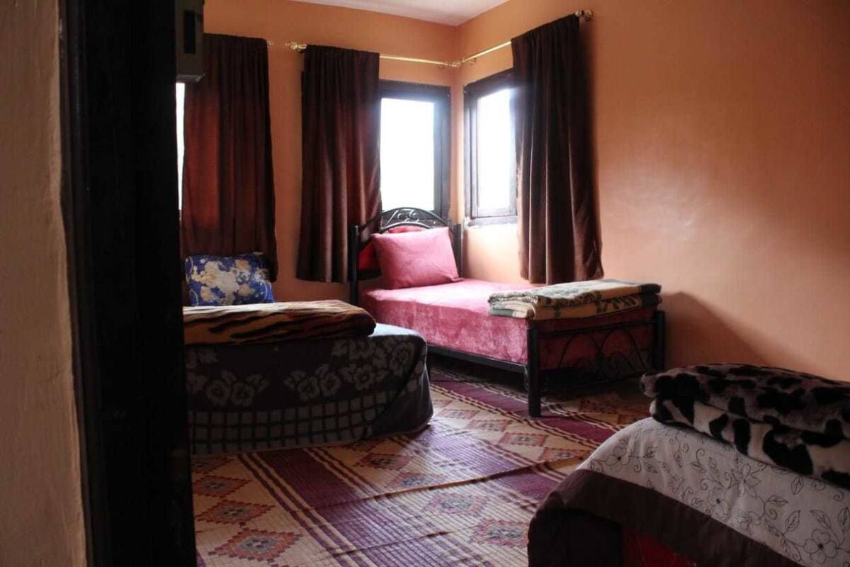 Ein Zimmer mit einem Bett, einem kleinen Tisch und einem Fenster mit Vorhängen.