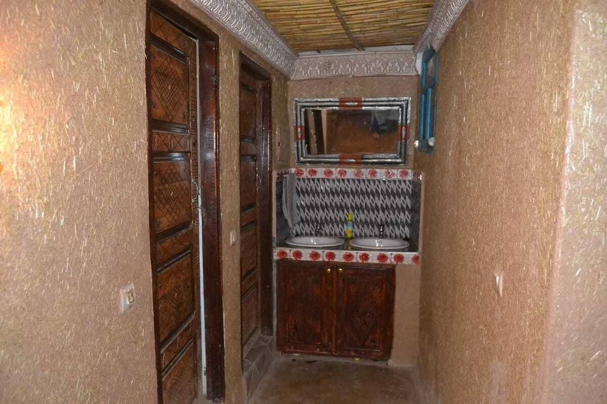 Ein schmaler Flur mit einer Holztür und einem kleinen Waschbereich mit Spiegel.
