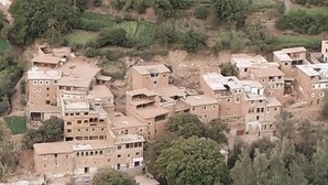 Eine Gruppe traditioneller Gebäude mit mehreren Stockwerken und flachen Dächern, umgeben von Grünflächen und terrassierten Feldern.
