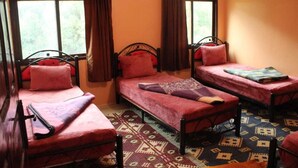 Ein Zimmer mit drei Einzelbetten, jeweils mit roter Decke und Kissen. Der Raum verfügt über einen gemusterten Teppich und große Fenster mit Vorhängen.