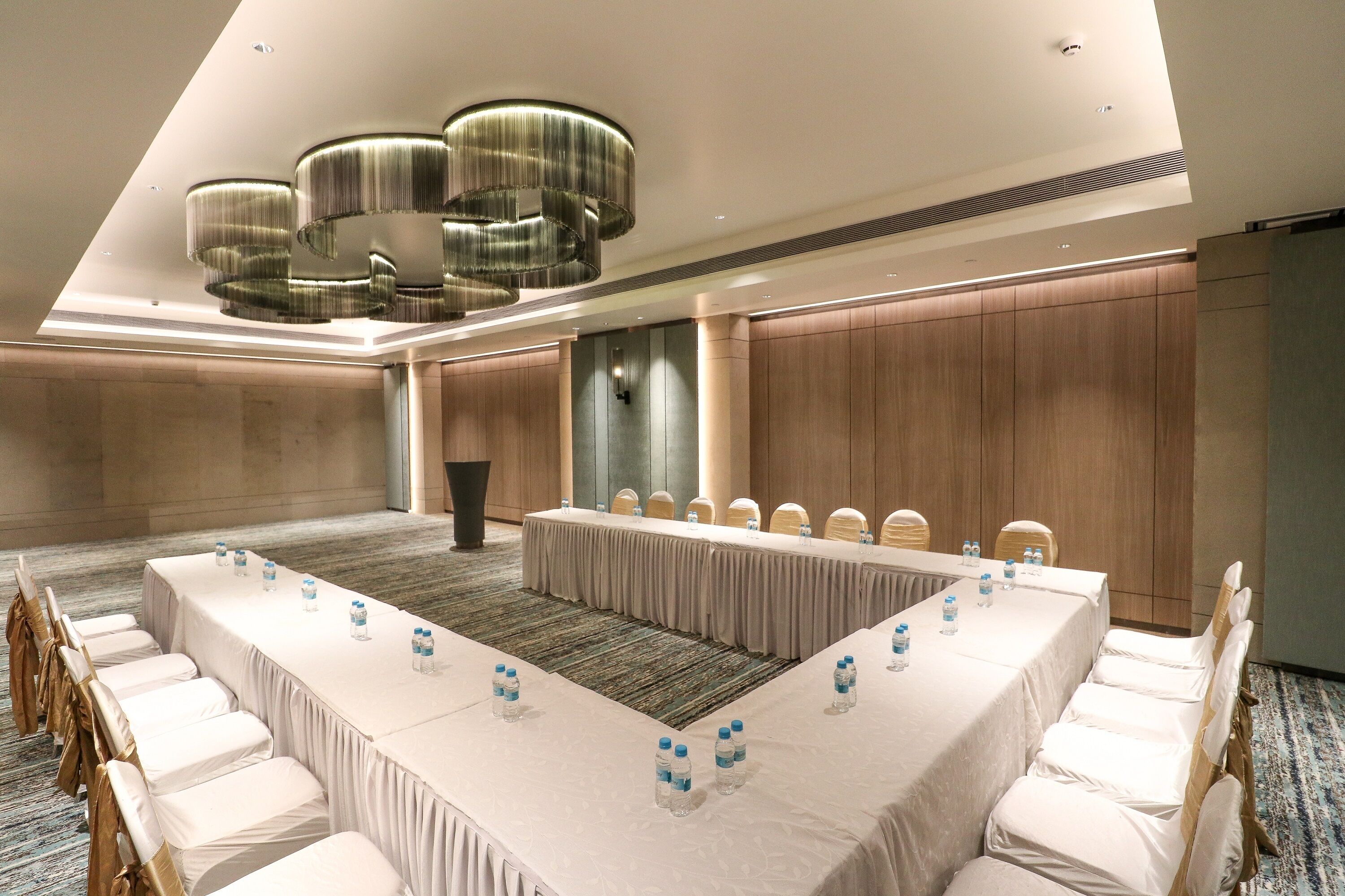 Une salle de conférence avec une longue table, des chaises blanches et des bouteilles d’eau.