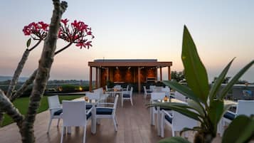 An outdoor seating area with white wicker furniture and a covered section with a view of the landscape.