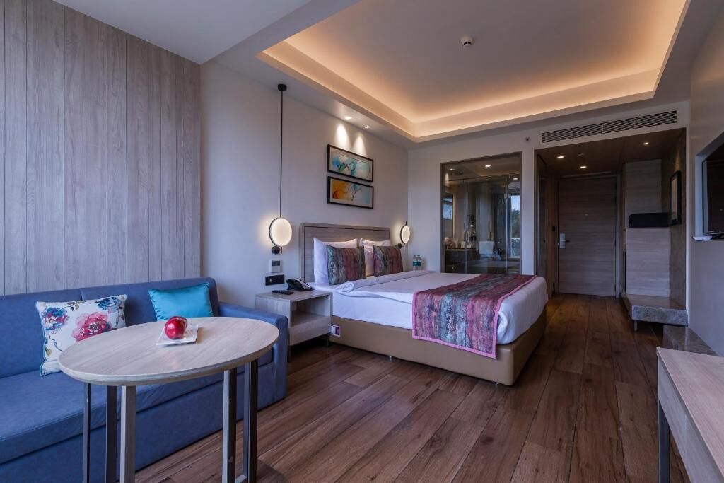 A modern hotel room with a bed, a sofa, a bedside table, and a small round table.