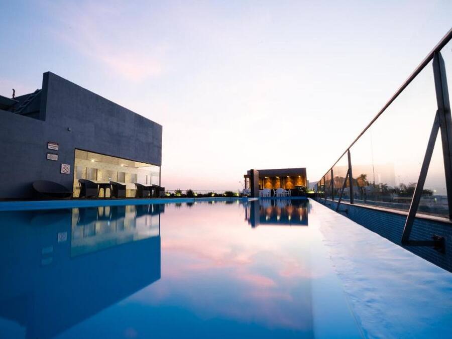 Un hotel moderno con piscina, una zona de estar al aire libre techada y vistas al atardecer.
