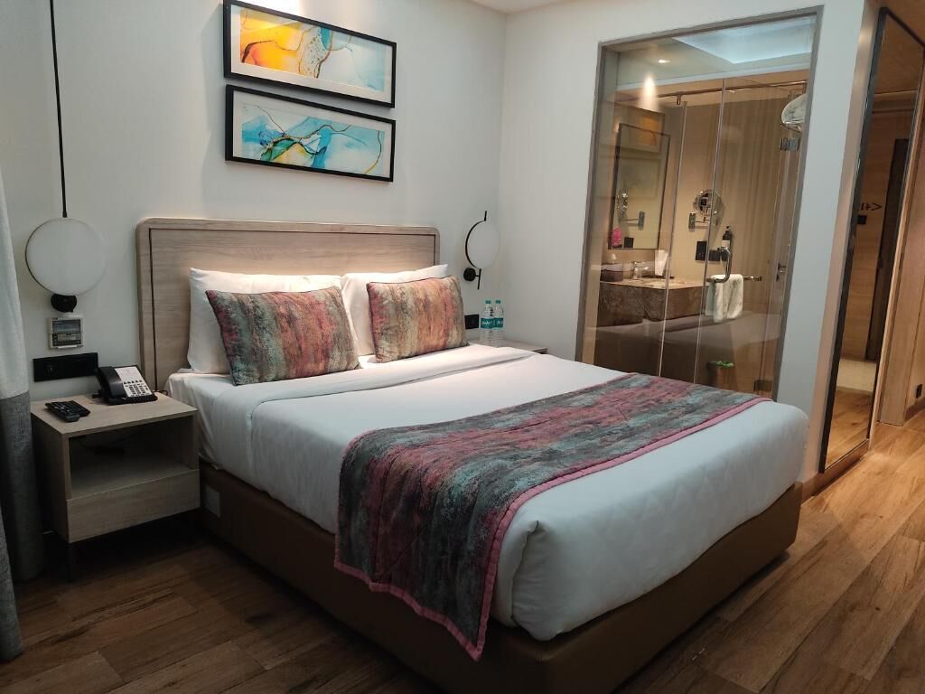 A hotel room with a bed, bedside table, and artwork on the wall.