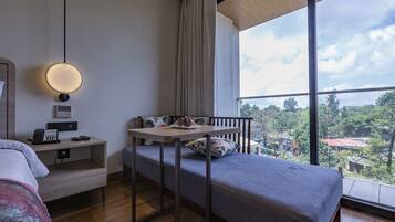 Ein Hotelzimmer mit einem Bett, einem Schreibtisch mit Lampe, einem Telefon und Blick auf die Stadt.