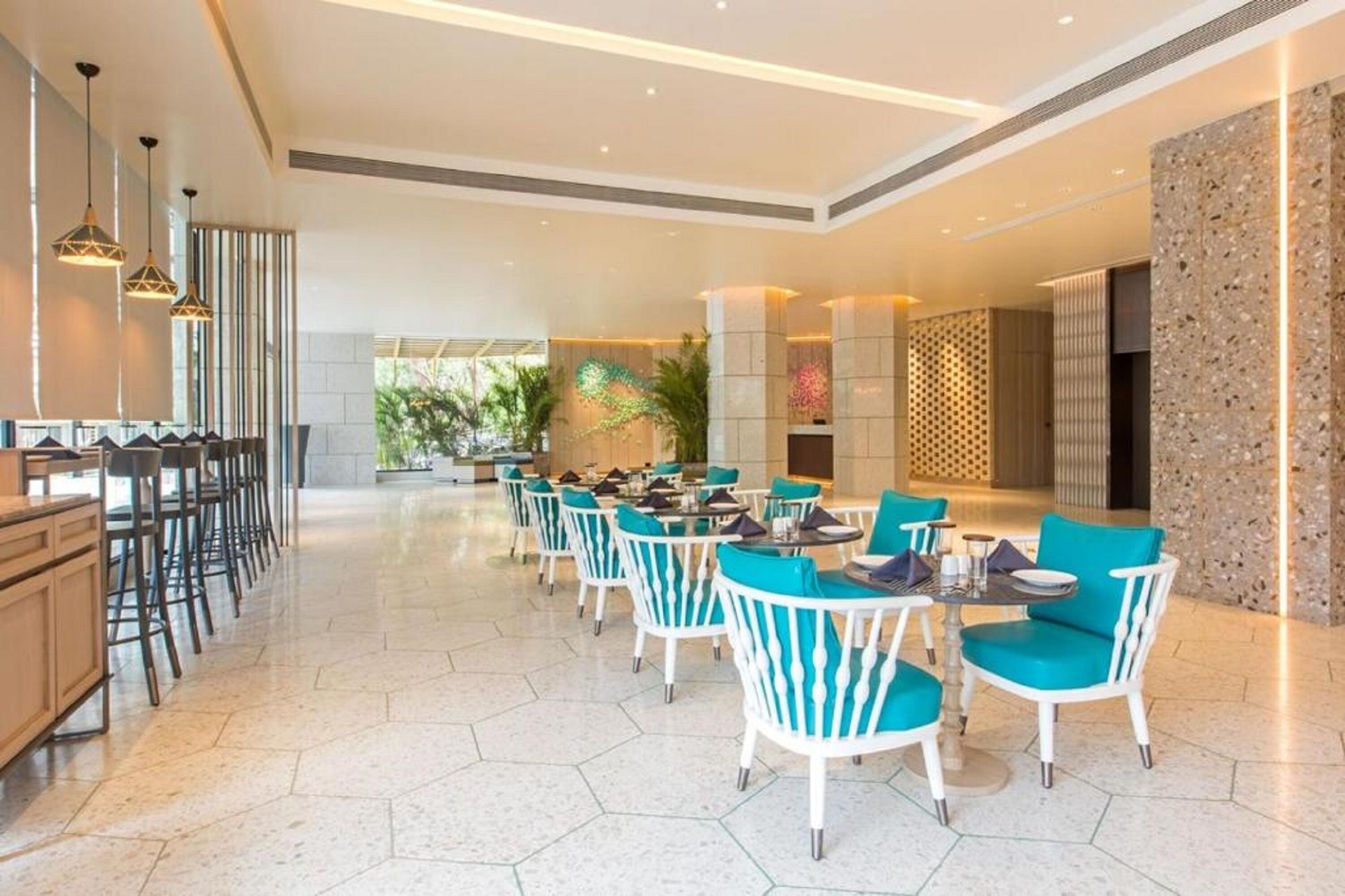 A spacious indoor area with multiple seating arrangements, including bar stools and tables with chairs, a reception desk, and a decorative wall with a textured pattern.