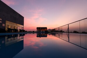 A modern building with a reflective pool in the foreground, a clear sky, and a distant mountain range. - Regenta SGS Greenotel - Lonavala (Mawal)