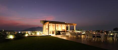 A modern outdoor dining area with a covered seating arrangement and a view of the mountains in the background.