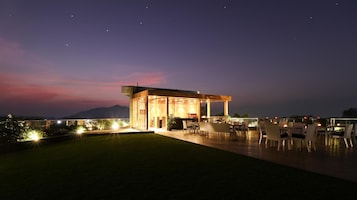 Un área de comedor exterior moderna con un espacio de estar techado y vistas a las montañas al fondo.