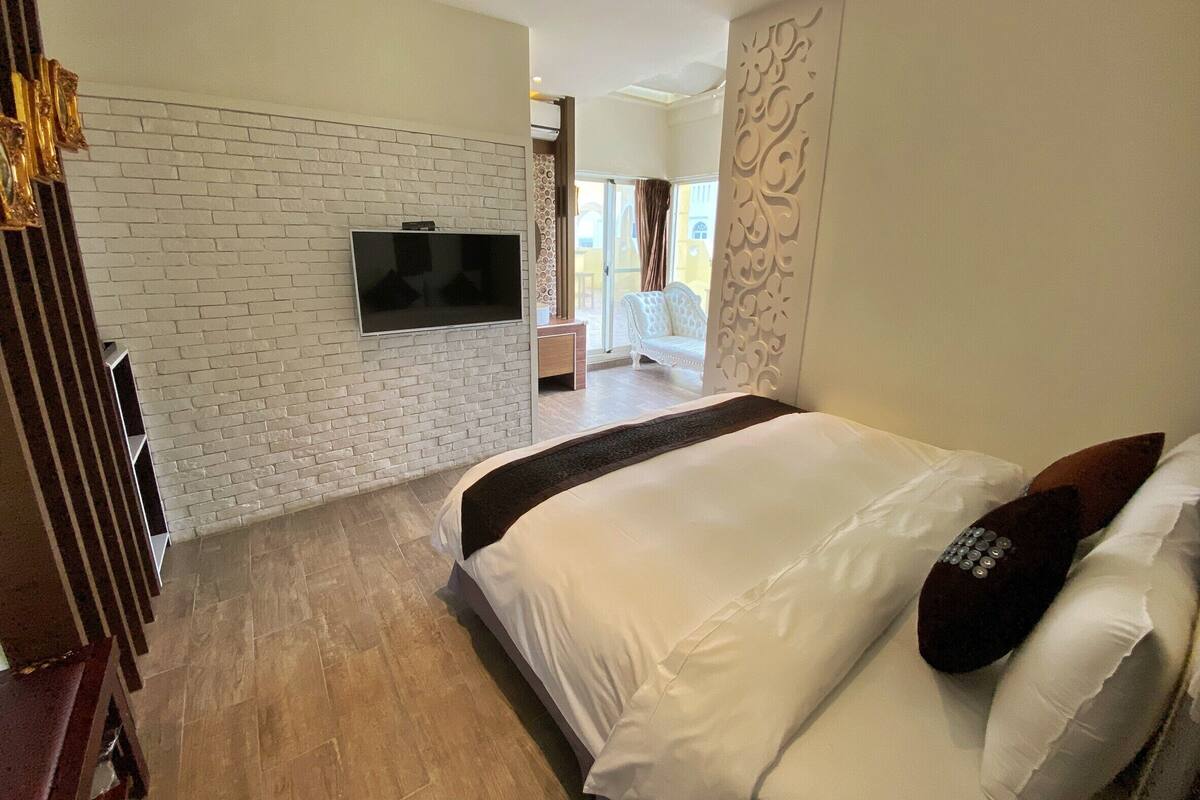 A hotel room with a brick wall, a flat-screen TV, a bed with white bedding, and a decorative wall panel.