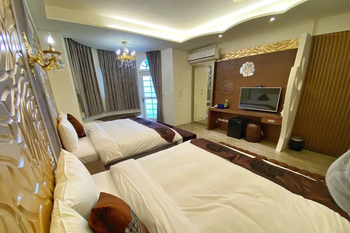 A hotel room with two beds, a TV, a minibar, and a large window with curtains.
