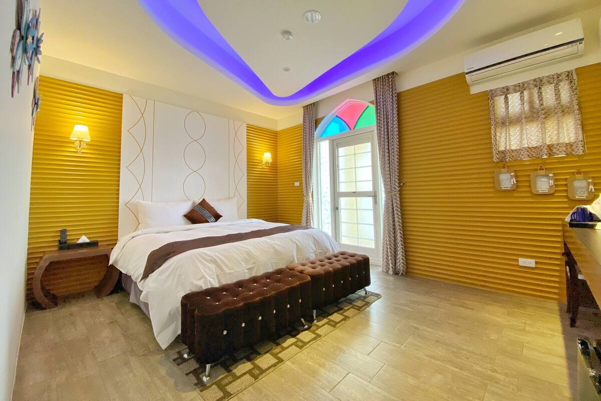 A modern bedroom with a bed, bedside lamps, a bench, and a window with curtains.