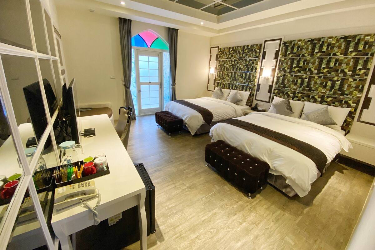A modern hotel room with two beds, a desk with a telephone, and a large window with a view of the outside.