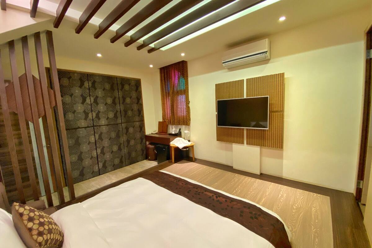 A modern hotel room with a large bed, a desk, a TV mounted on a textured wall, and an air conditioning unit.