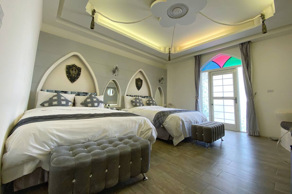 A bedroom with two beds, a decorative ceiling, and a window with curtains.
