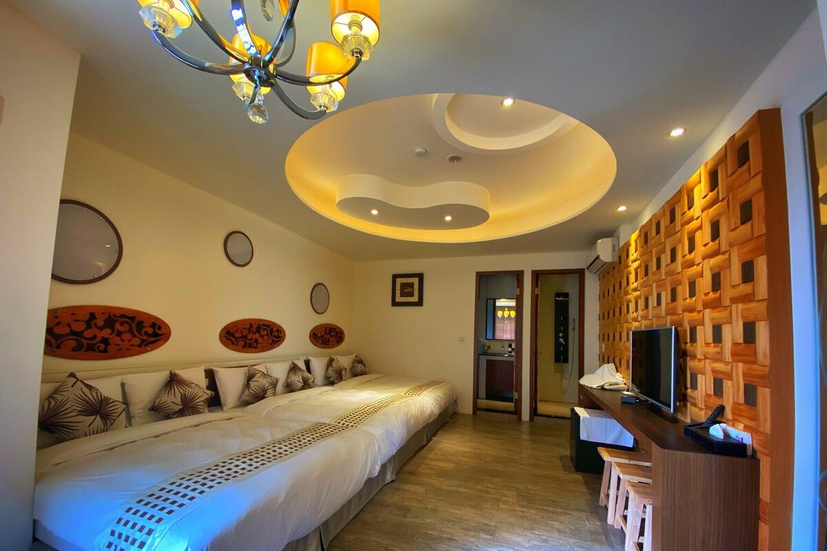 A modern hotel room with a large bed, a TV, a wooden accent wall, and a ceiling light fixture.