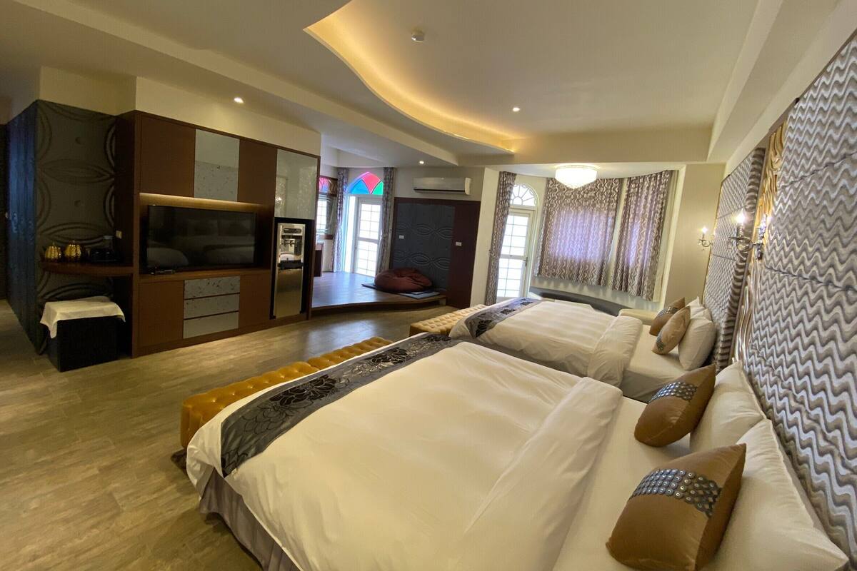 A spacious bedroom with a large bed, a wardrobe, a seating area, and a television.