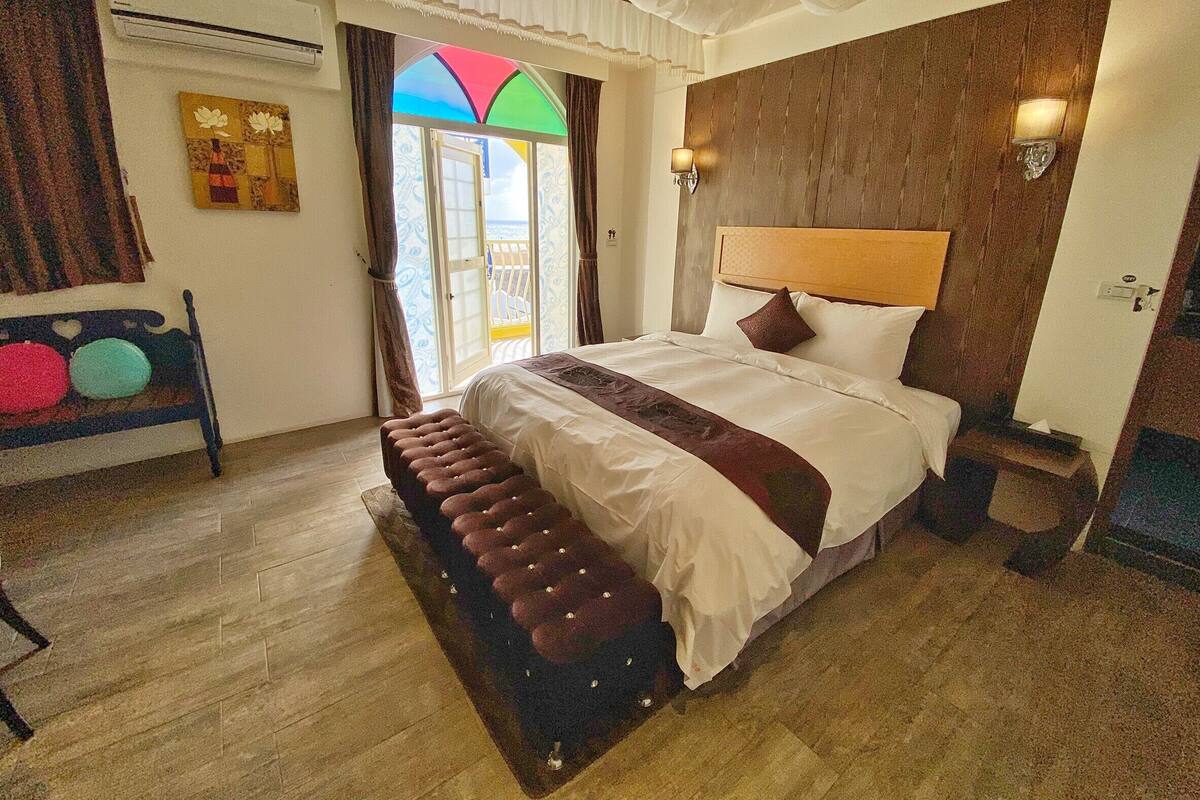 A bedroom with a large bed, a bench, a view of the sea, and a wooden wall.