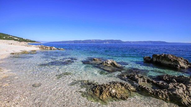A clear coastal beach with rocky formations and a distant mountain range. - Villa Aida (Labin)