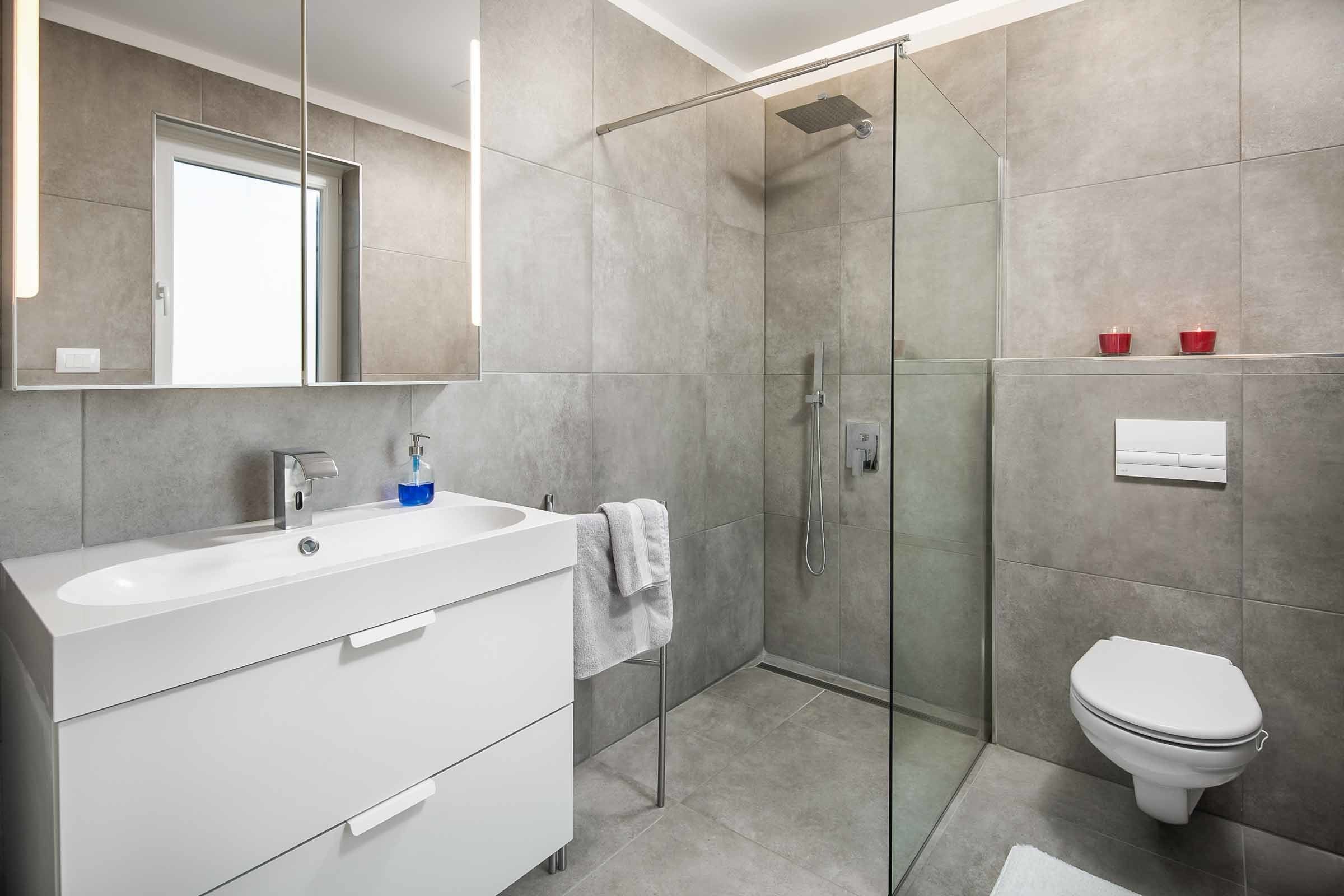 A modern bathroom with a glass shower enclosure, a white sink with a mirror, and a toilet.