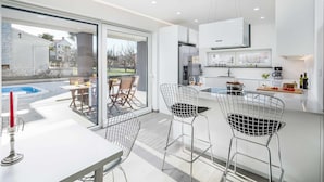 A modern kitchen with a large island, bar stools, and a view of a swimming pool. - Villa Aida (Labin)