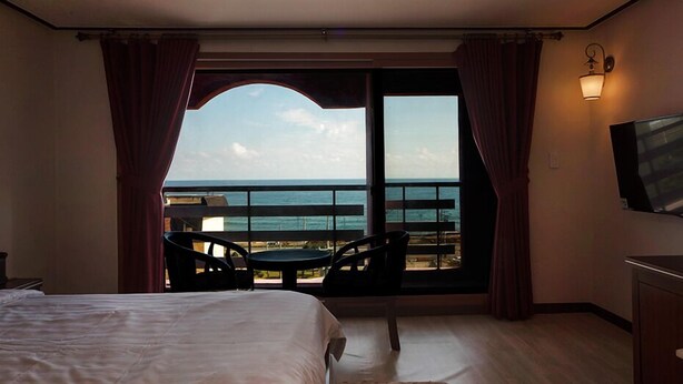 Una habitación de hotel con una cama grande, un balcón con mesa y sillas, y un televisor.