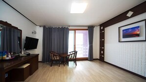 Una habitación con un escritorio de madera, una silla, un televisor, una ventana con cortinas y un cuadro en la pared.