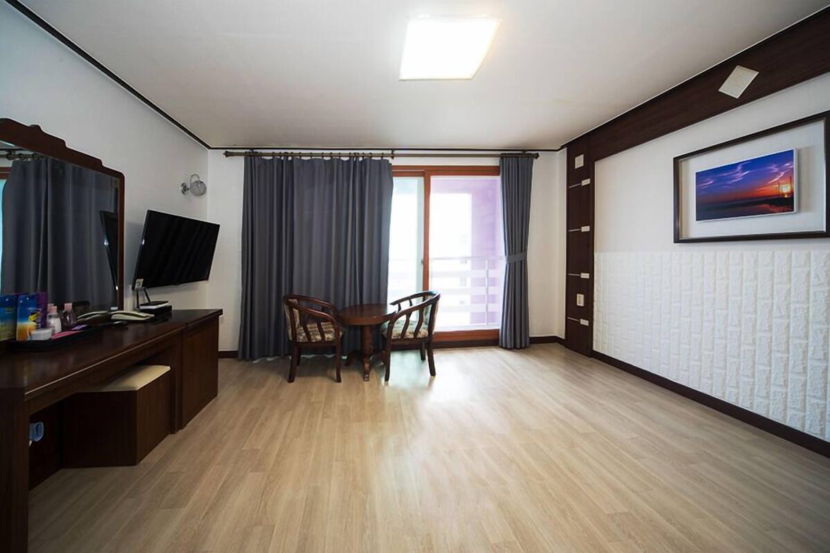 Una habitación con un escritorio de madera, una silla, un televisor, una ventana con cortinas y un cuadro en la pared.