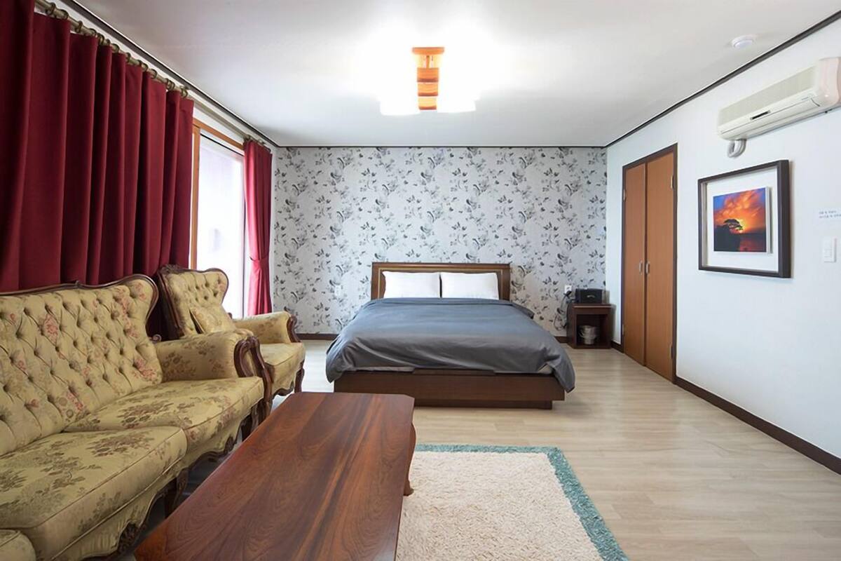 Un dormitorio con cama, sofá, mesa de madera y ventana con cortinas.