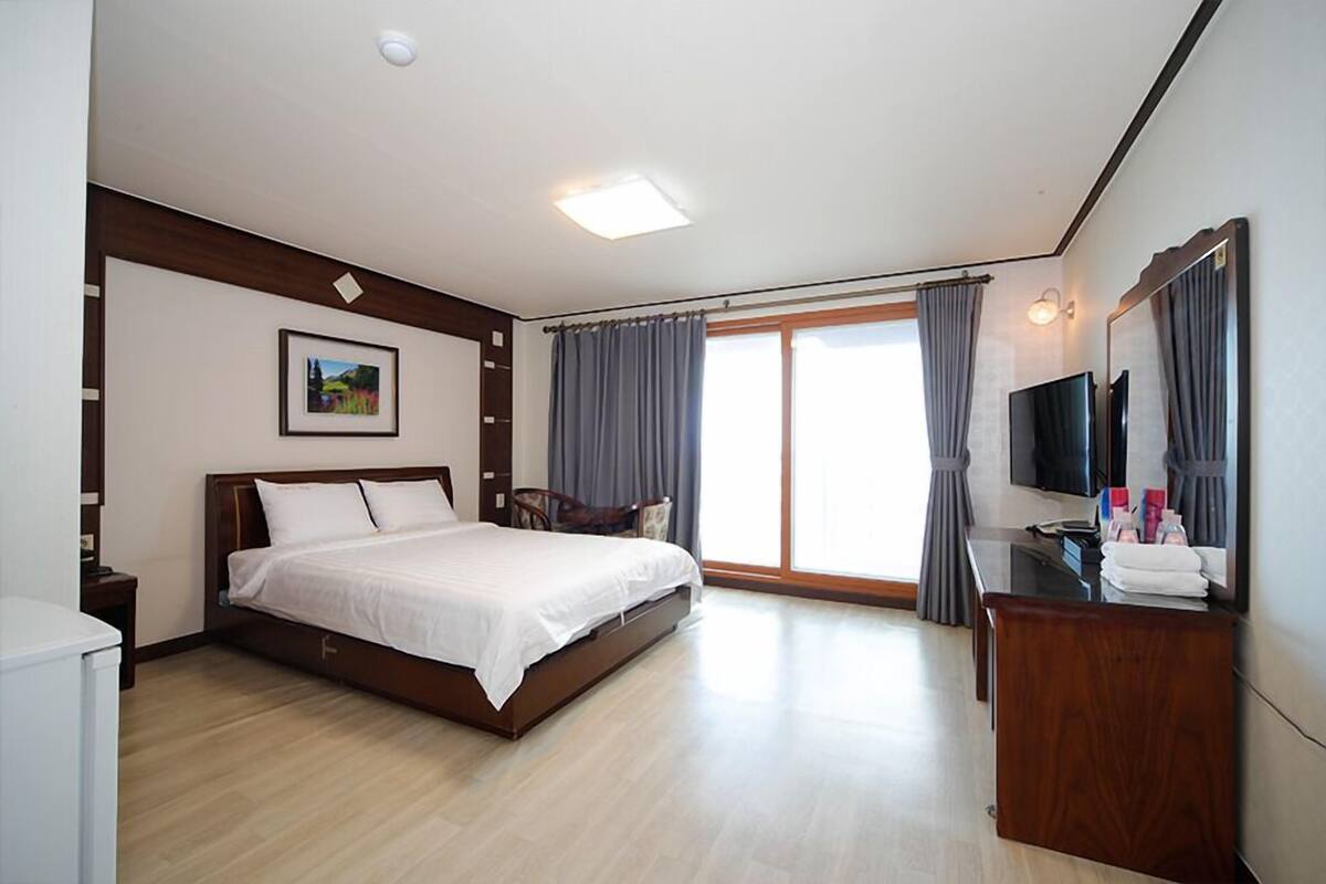 Una habitación de hotel con cama, escritorio, silla, televisor y ventana con cortinas.