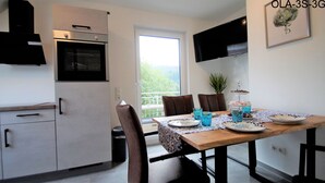 A compact kitchen with a built-in oven, a dining table set with plates and glasses, and a potted plant. - Overath Luxus Apartments (Overath)