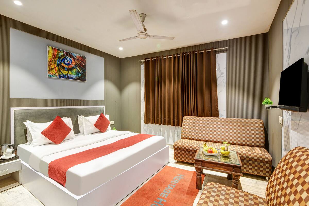 A modern hotel room with a large bed, a sofa, a coffee table, and a TV.