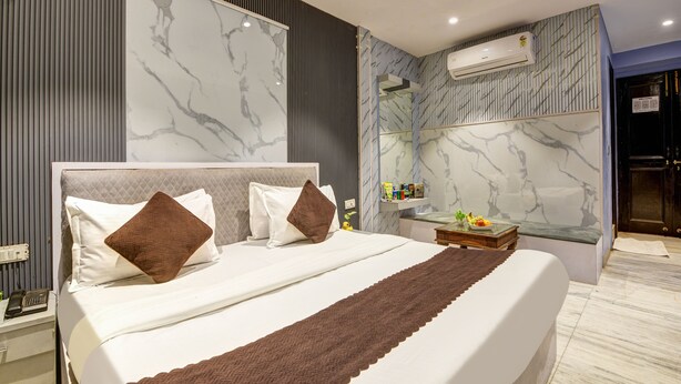 Habitación de hotel moderna con una cama grande, paredes con diseño de mármol, un banco integrado y una pequeña mesa con artículos de cortesía.